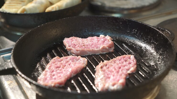 Koki menyiapkan daging lezat di wajan panggangan. Steak sempurna