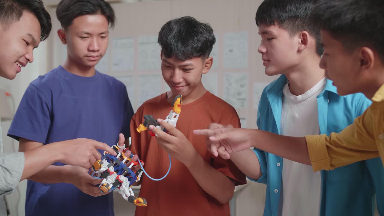 grupo de jóvenes chicos asiáticos con una computadora portátil e impresión 3d ayudándose unos a otros a montar una mano de cyborg mientras trabajan en casa