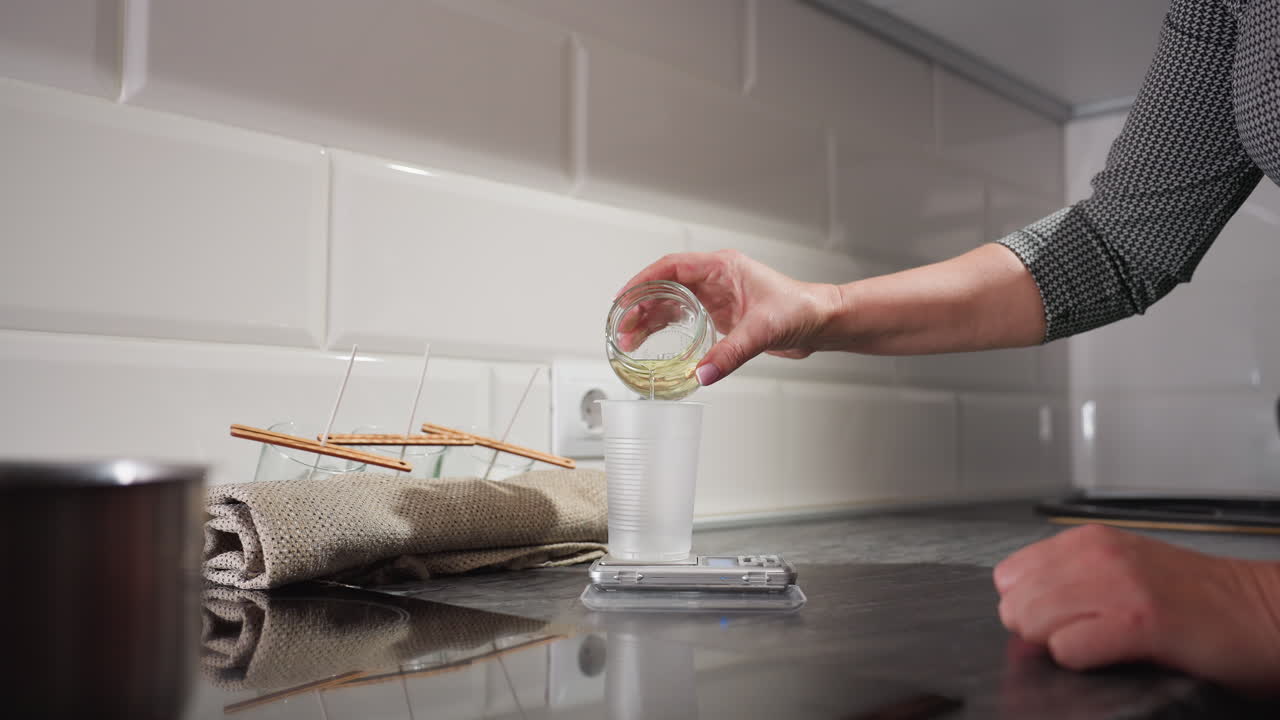 Plastic cup placed on scale, liquid being poured into the cup to measure weight accurately, as part of candle making or liquid measuring process in kitchen
