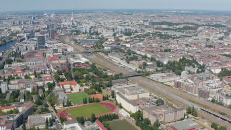 Tilt-up-reveal-cityscape.-Aerial-view-of-large-city,-multitrack-railway-line-running-through-urban-neighbourhood.-Berlin,-Germany