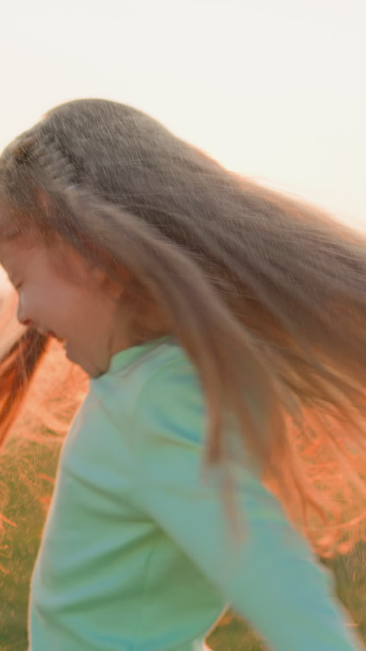 강변에서 비가 내리면서 행복한 아이가 춤을 추고, 긴 느슨한 머리카락을 가진 즐거운 어린 소녀가 여름날에 떨어지는 비방울에서 놀고, 폭풍우를 축하합니다.