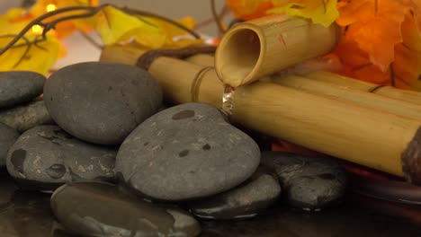 Water-fountain-pouring-water-of-rocks-with-fall-leaves-in-the-background