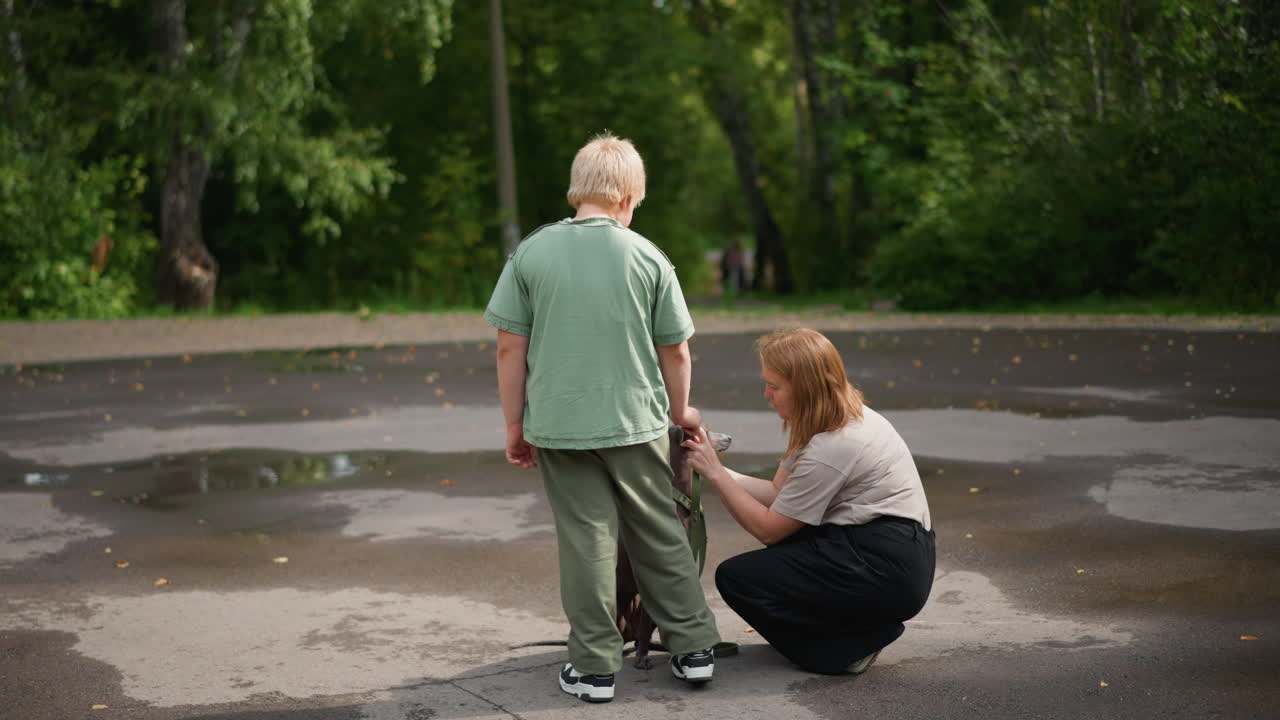 Woman Helps Boy Put On Shoes During Wet Weather, Mother Assists Her Young Son With Footwear On Rainy Day, Caring Woman Helps Boy With His Shoes While Standing Outside In Rainy Conditions