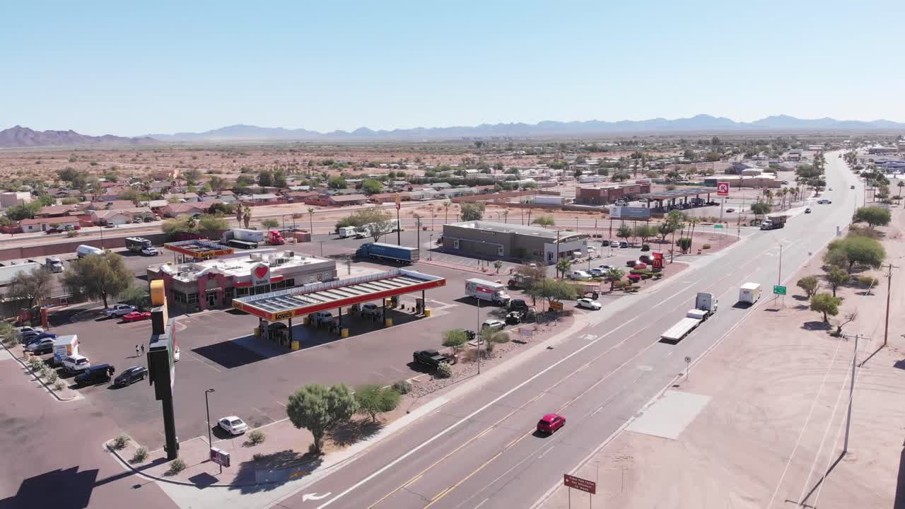 Flight towards desert truck and vehicle gas station and restroom depot stop with mountain range in background, aerial approach