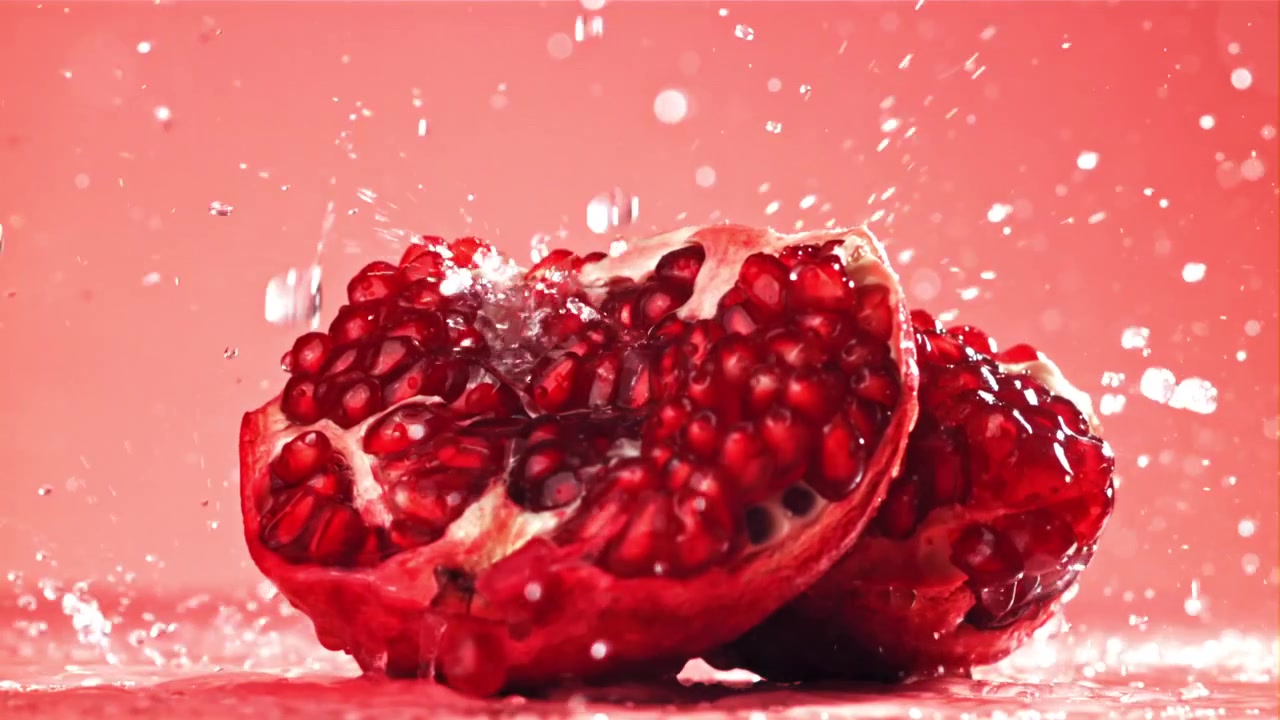 Saftige granatæblehalvdele oversprøjtet med vand i slowmotion