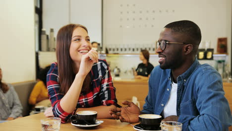 caucasian woman and african american man talking sitting at a table in a cafe