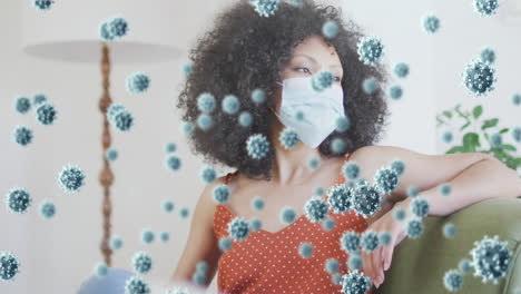 animación de células de coronavirus sobre una mujer afroamericana que usa una máscara facial en casa
