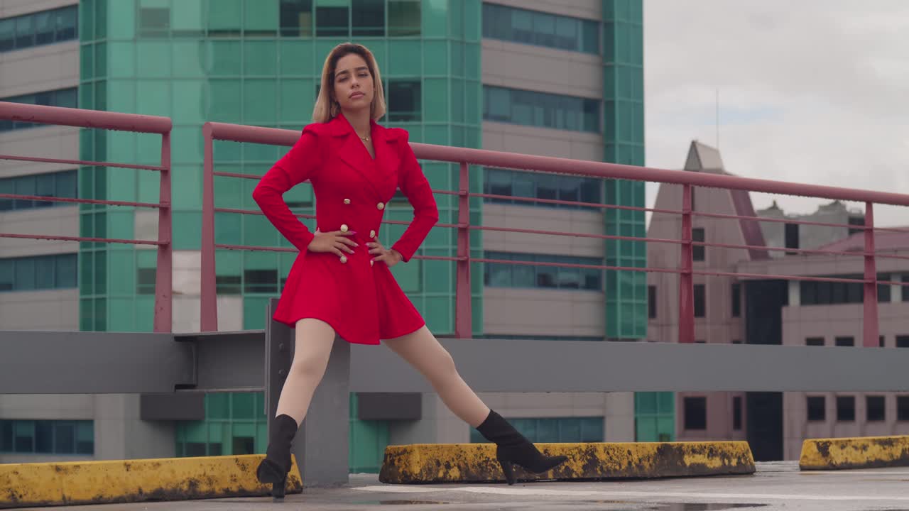 A Port of Spain, Trinidad, una giovane ragazza ispanica siede su un tetto con un vestito rosso, con alti edifici in lontananza