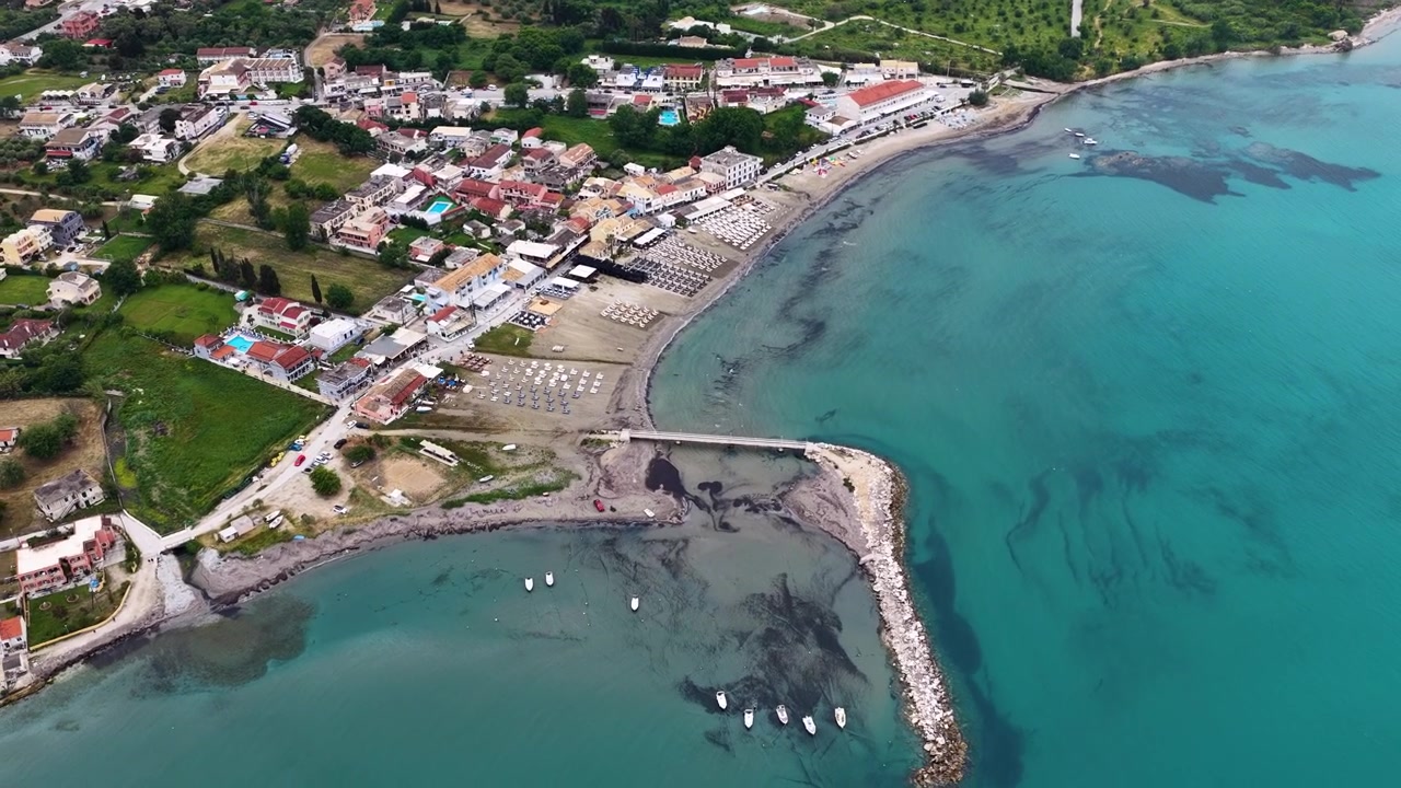 Panorama aereo della costa del villaggio di Roda a Corfù Nord, Grecia. Vista drone del Mar Ionio, spiaggia sabbiosa, lettini, hotel e molo frangiflutti durante una vacanza estiva.