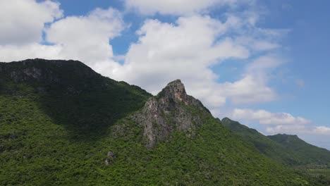 un metraje aéreo constante de esta montaña cubierta de árboles y una torre de roca que sobresale con un hermoso cielo azul y nubes en movimiento, parque nacional sam roi yot, prachuap khiri khan, tailandia