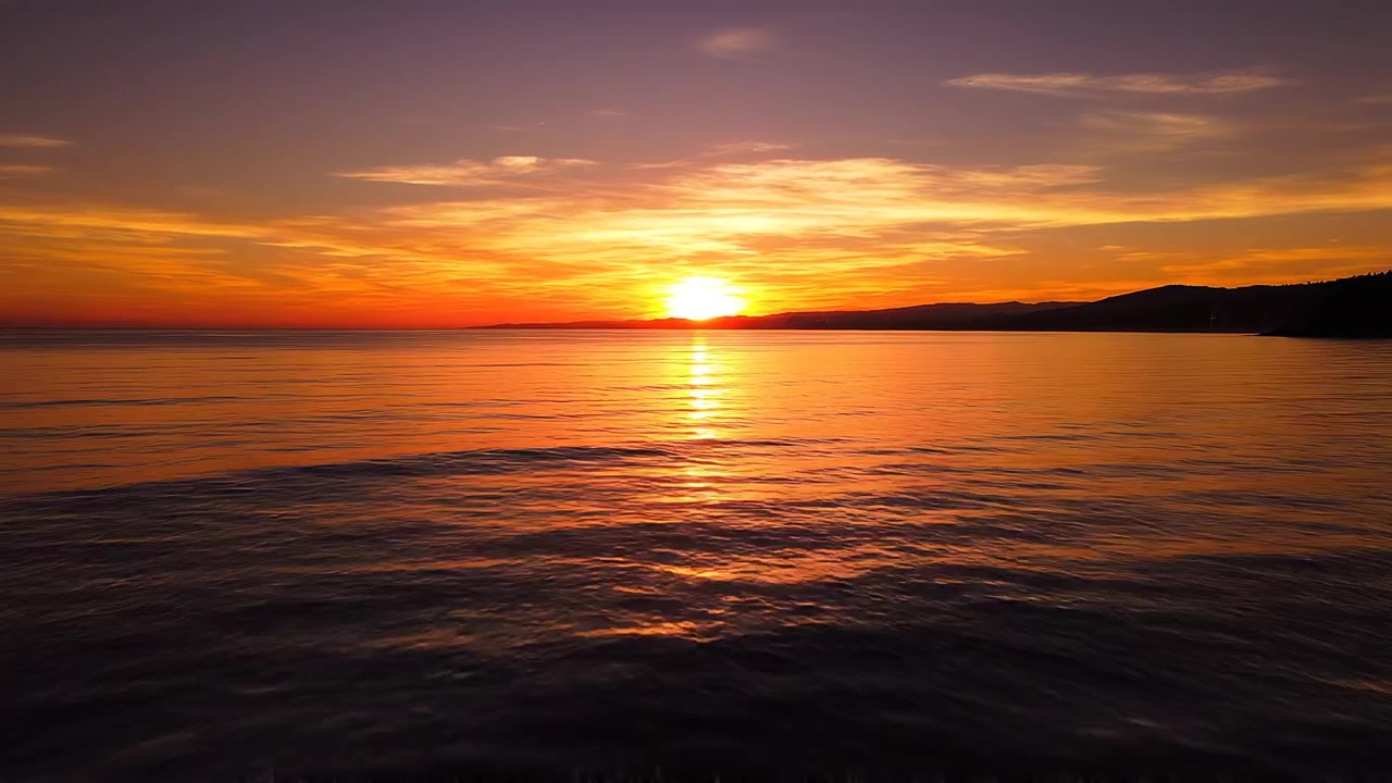 Matahari Terbenam Keemasan yang Indah di Atas Laut Tenang dengan Cakrawala Pegunungan