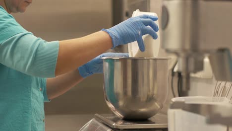 woman baker pouring flour into bowl standing on kitchen scale in restaurant