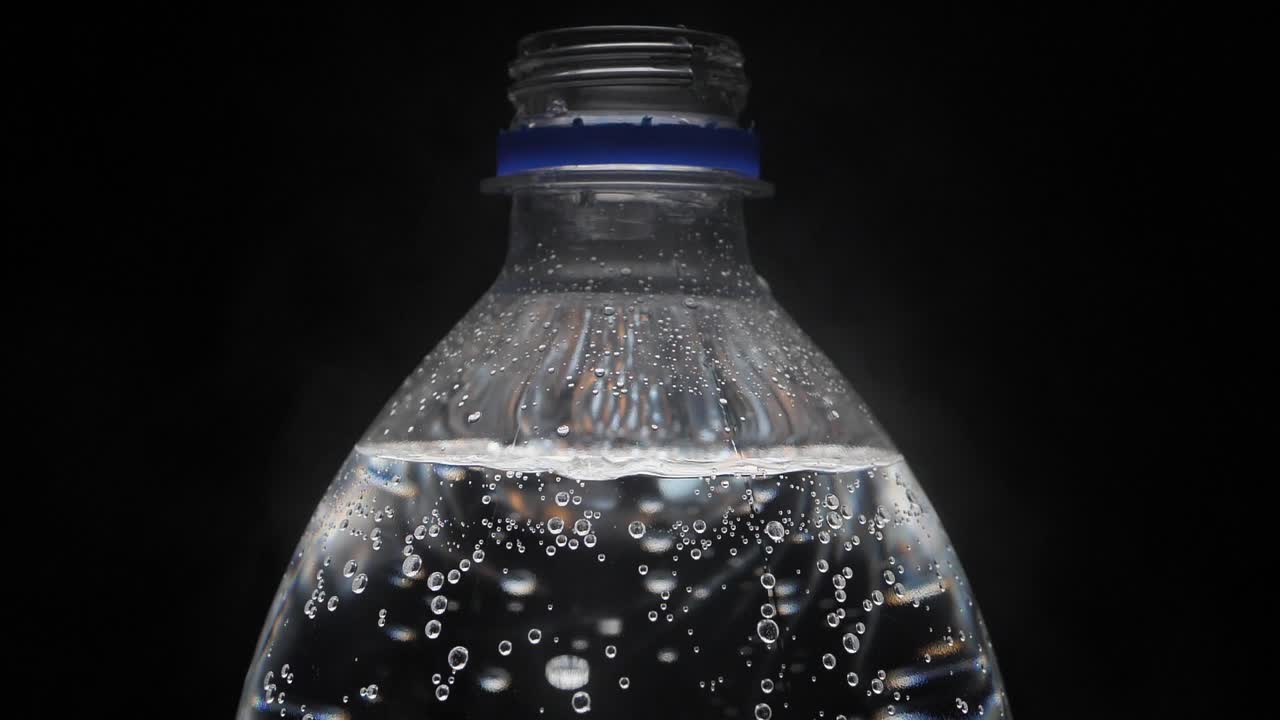 una botella de agua carbonatada se desenrosca a mano sobre un fondo negro