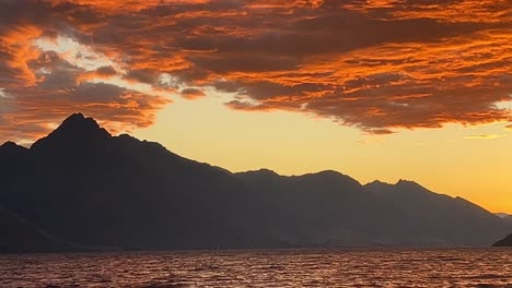 Vibrantly-coloured-sunset-clouds-over-rugged-mountain-peak-in-Queenstown,-New-Zealand