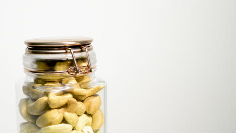 Roasted-cashews-in-a-jar,-rotating-slowly-against-a-white-background