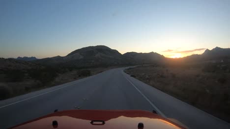 driving toward the sunrise in a red vehicle in the desert with mountains visible in silhouette