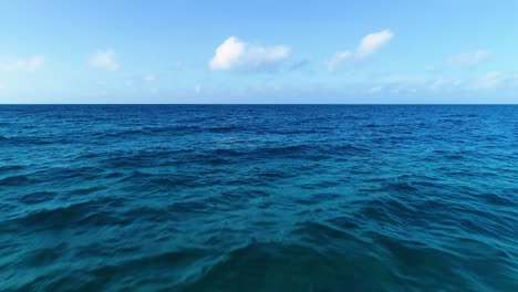 Drone-dolly,-blue-sky-white-clouds-above-calm-ocean-reef-to-drop-off