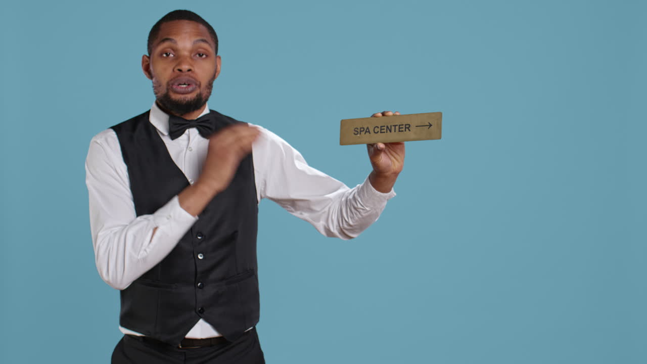 Hotel employee in tuxedo pointing people to the spa center using a wall sign