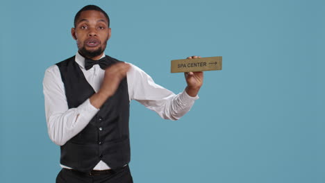 hotel employee in tuxedo pointing people to the spa center using a wall sign