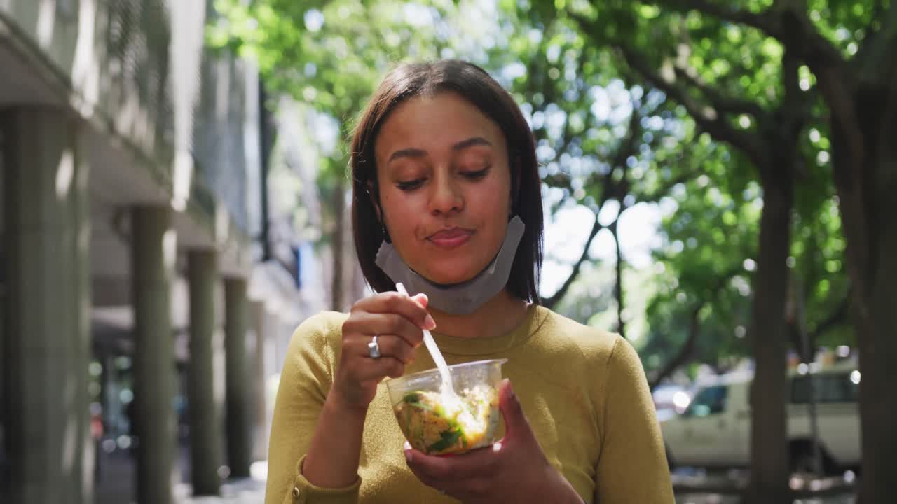 mujer afroamericana con máscara facial comiendo ensalada en el parque de la ciudad