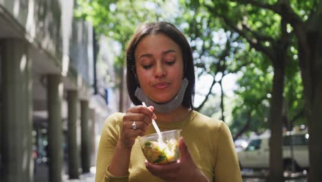 african american woman wearing face mask eating salad in sity park