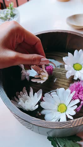 la mano de la mujer tocando suavemente las flores en un cuenco de madera