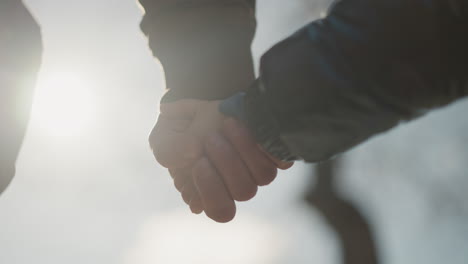 adult and a child holding hands, illuminated by the soft glow of sunlight as he gently squeeze the child hand, with blurred view of a tree