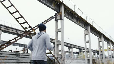 vista trasera de un joven deportista con capucha gris trotando en las ruinas de una antigua fábrica en una mañana nublada