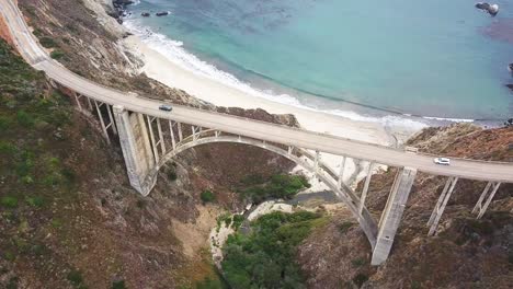 aerial backward reveal from seaside cliff to bixby bridge and car traffic