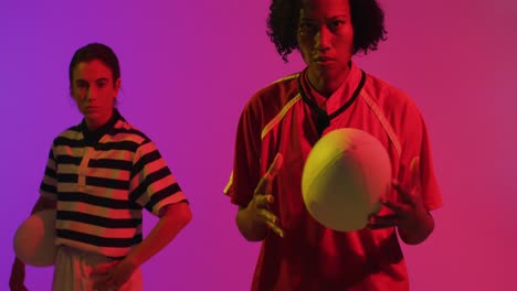 portrait of diverse female rugby players with rugby balls over neon pink lighting