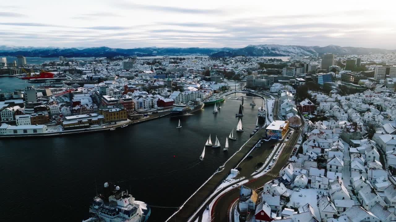 Talvinen, elokuvamainen ja ilmasta kuvattu drone-kuvamateriaali Stavangerin keskustasta Norjassa. Lumipeitteiset katot ja purjeveneet liikkuvat satamakanavassa. Kamera liikkuu tasaisesti ylhäältä alas.