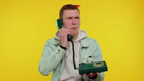 Crazy-sincere-teen-man-talking-on-wired-vintage-telephone-of-80s,-fooling,-making-silly-funny-faces