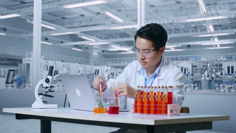 アジア人の男性科学者が試管で実験を行いラップトップでマイクロスコープでタイピングしている様子実験室で作業し試管のサンプルを見つけている様子