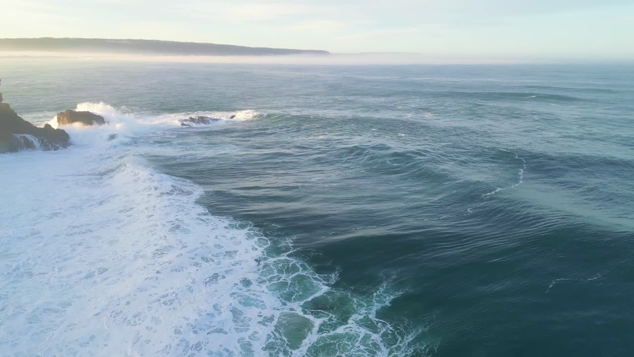 Waves crashing against the rocks near the iconic lighthouse in Nazare, Portugal