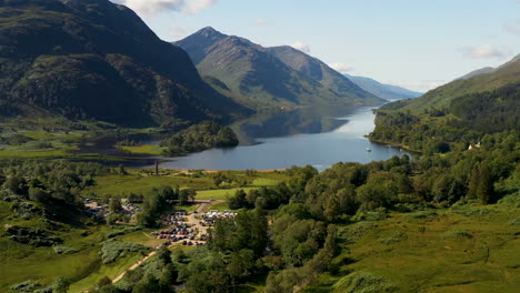 Toma-Cinematográfica-De-Drones-Del-Viaducto-De-Glenfinnan-Con-Agua-Y-Montañas-En-El-Fondo