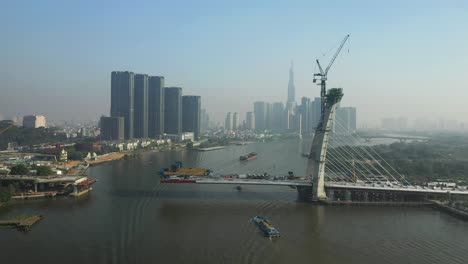 Drone-view-of-Saigon-River,-Ho-Chi-Minh-City-and-new-Thu-Thiem-Bridge-under-construction-on-a-sunny-day