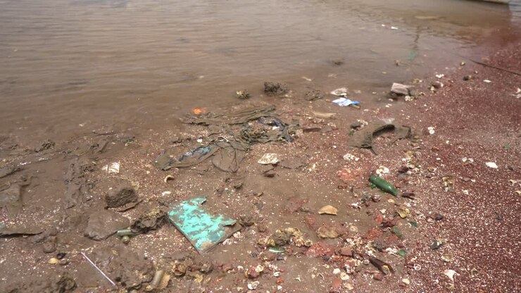 A littered beach with scattered debris and a distant rocky shoreline on a cloudy day
