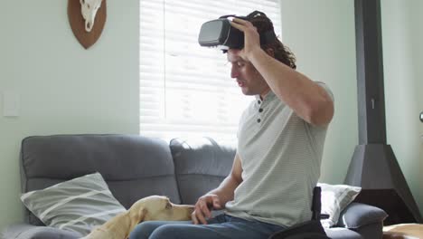 hombre discapacitado caucásico feliz en silla de ruedas con auriculares vr jugando con perro mascota en la sala de estar