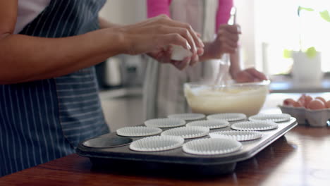 sección media de madre e hija biraciales haciendo pasteles en la cocina, espacio de copia, cámara lenta