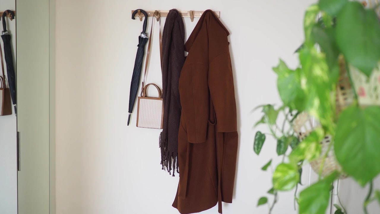 Cappotto marrone e accessori appesi a un gancio a muro in un ingresso minimalista