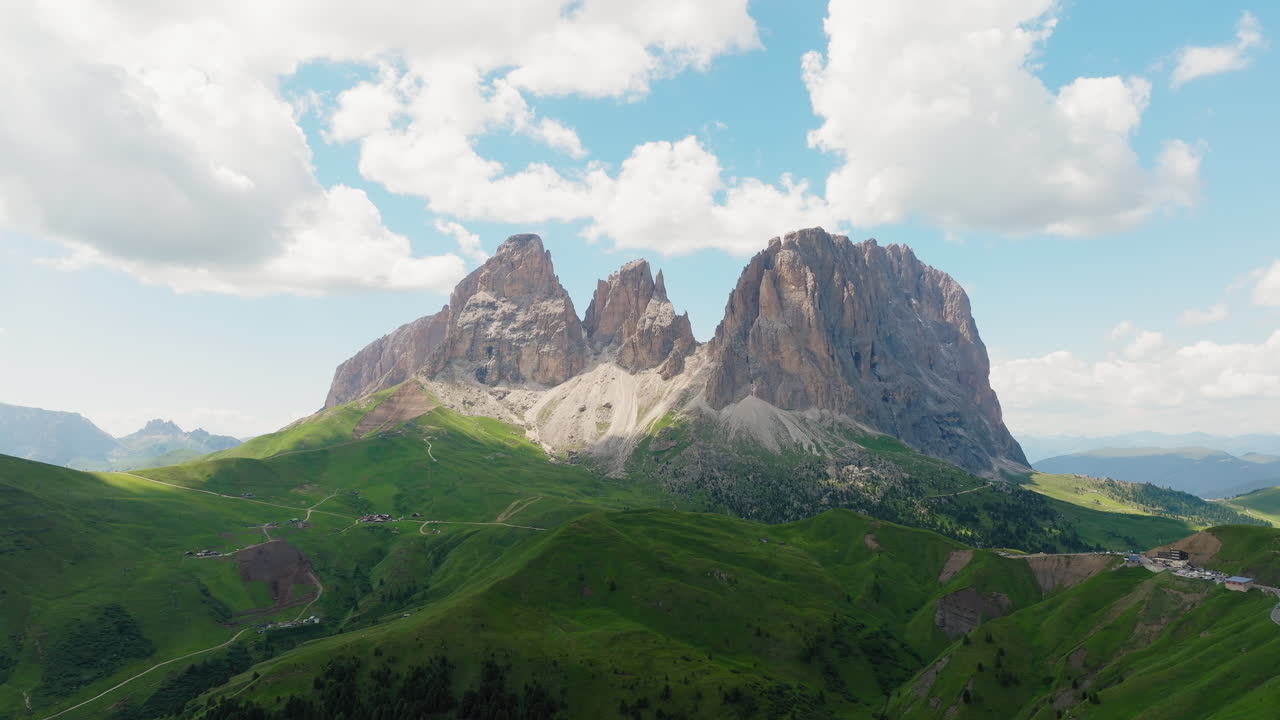 Aerial of Sassolungo massif in Dolomites with vibrant meadow and curving dirt road