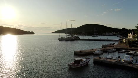 a drone flying towards a couple of sailboats docked on a stone pier