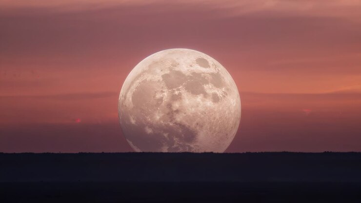 Lua cheia nascendo e se movendo para cima durante o pôr do sol sobre o horizonte ao crepúsculo, mostrando crateras, luz vermelha