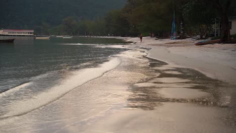 Kleine-Wellen-Des-Sich-Spiegelnden-Meeres-Rollen-über-Den-Wunderschönen-Sandstrand-Von-Koh-Rong-Sanloem,-Während-Eine-Frau-Auf-Koh-Rong-Sanloem-Läuft