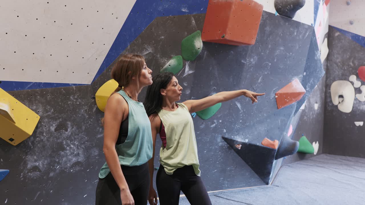 mujeres irreconocibles de pie cerca de la pared de escalada en el gimnasio