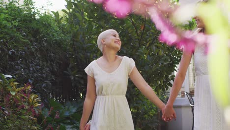 Happy-diverse-female-couple-holding-hands-and-walking-in-garden