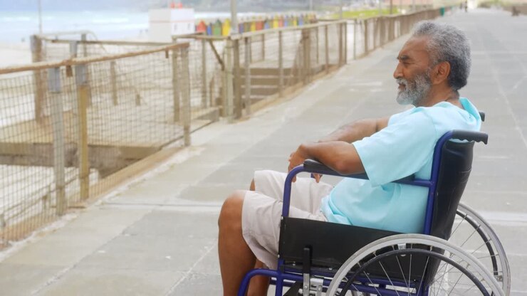 Vista laterale di un anziano afroamericano disabile attivo e pensieroso in sedia a rotelle sul lungomare, 4K.