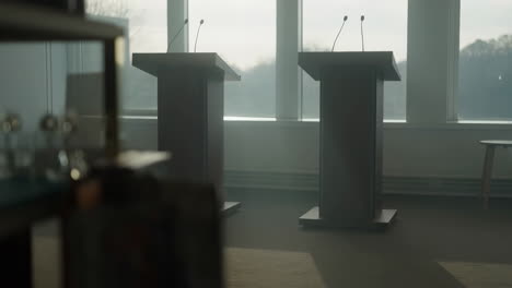 two podiums with microphones set up in front of large windows for a debate or conference