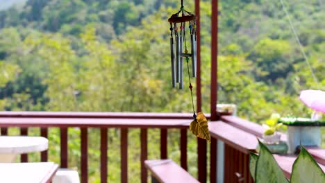 a wind chime gently sways on a balcony overlooking lush greenery in phuket, thailand, under bright daylight