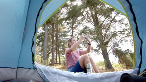 young caucasian woman captures a moment with her phone inside a tent